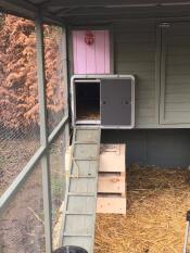 An Autodoor attached to a large wooden chicken coop with a ramp up to the door