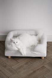 A white cat enjoying the comfort of his white bolster bed