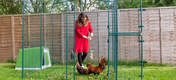 Omlet green Eglu Go plastic chicken coop in Omlet walk in chicken run with chickens and lady holding Omlet Caddi treat holder