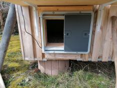 Omlet grey automatic chicken coop door attached to wooden chicken coop