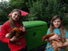 Two girls holding chickens next to their chicken coop