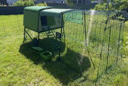 A green chicken coop with a run in a garden