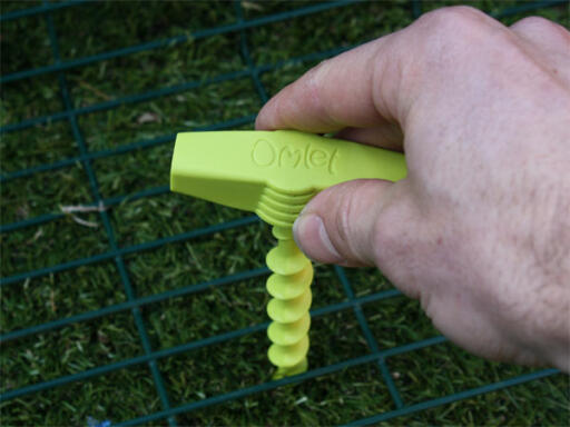 Green Omlet screw peg being screwed into ground to hold run down
