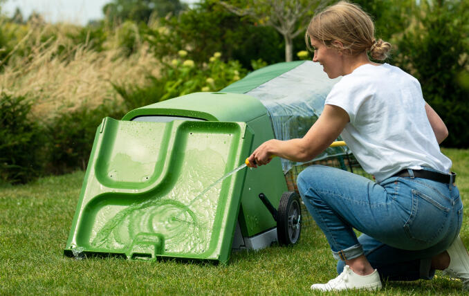 A woman cleaning her Eglu Go Hutch with a hose.