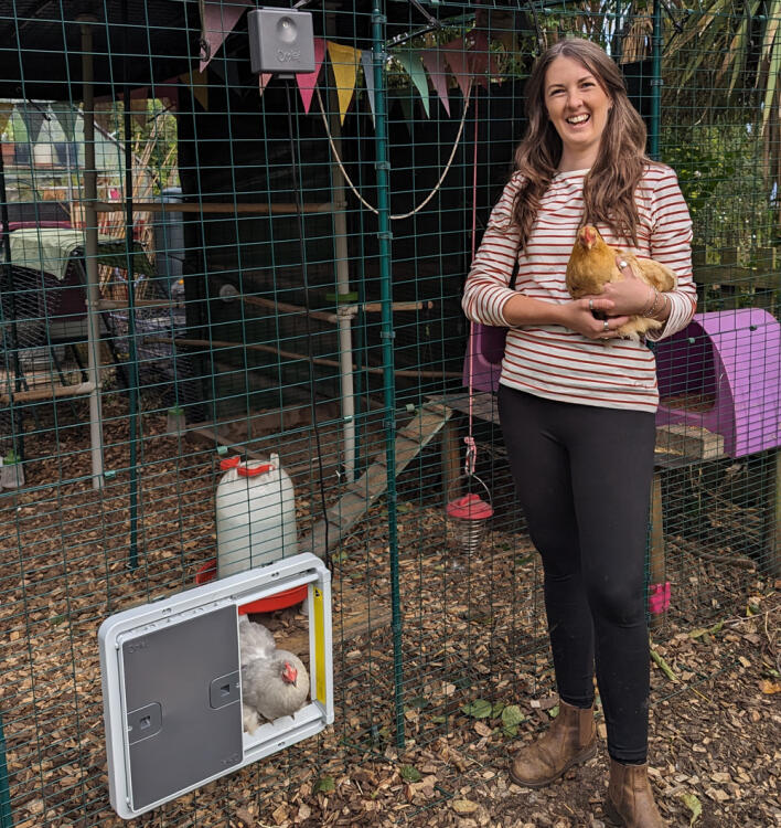 Woman holding a chicken in front of her chicken run with automatic coop door