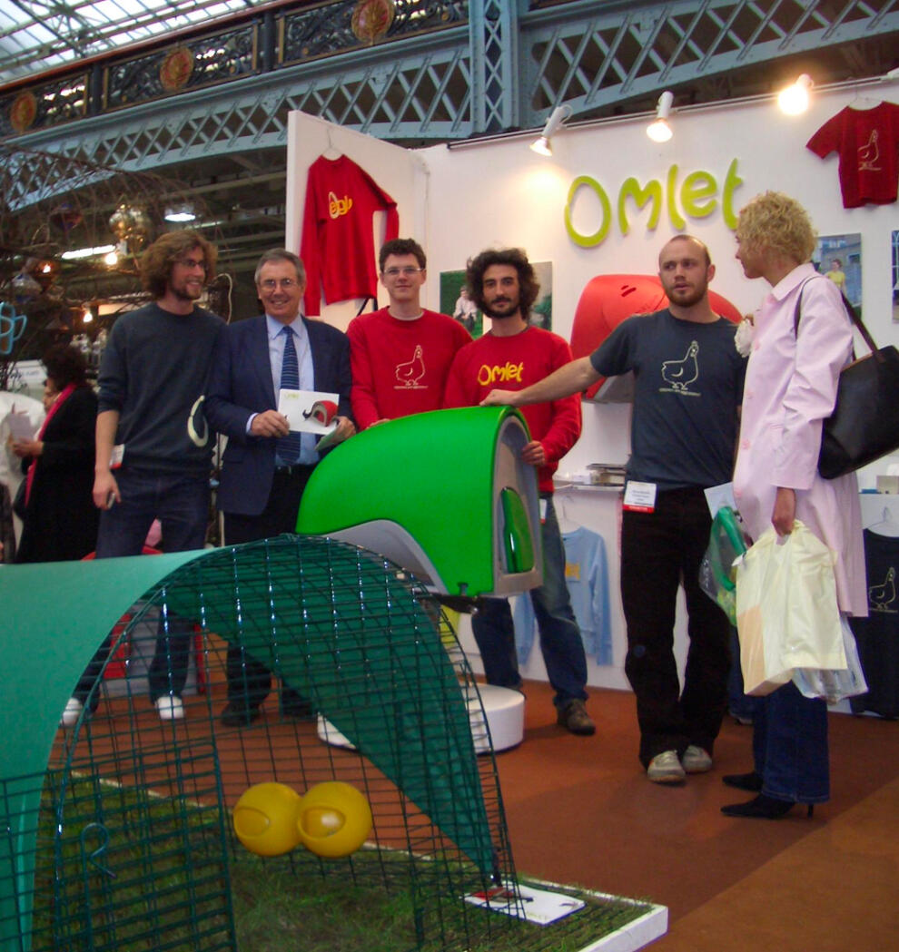 A group of people posing at a stand with the Eglu Cube chicken coop