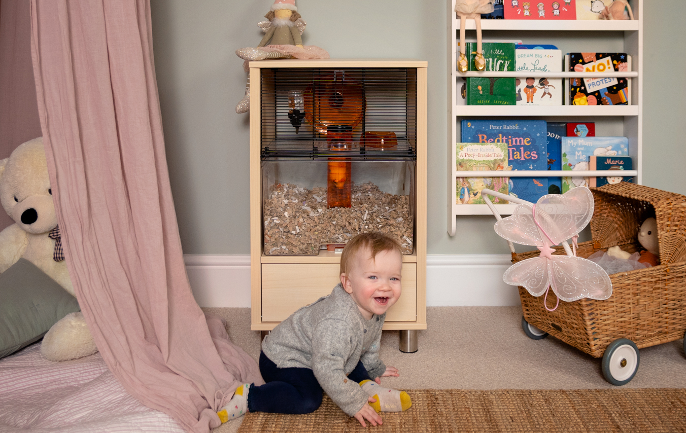 Toddler playing in a bedroom with a hamster cage in the background