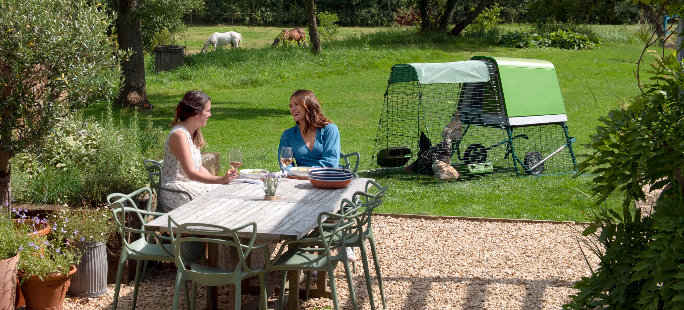 Two women having lunch in a garden near an Eglu Go Up Chicken Coop