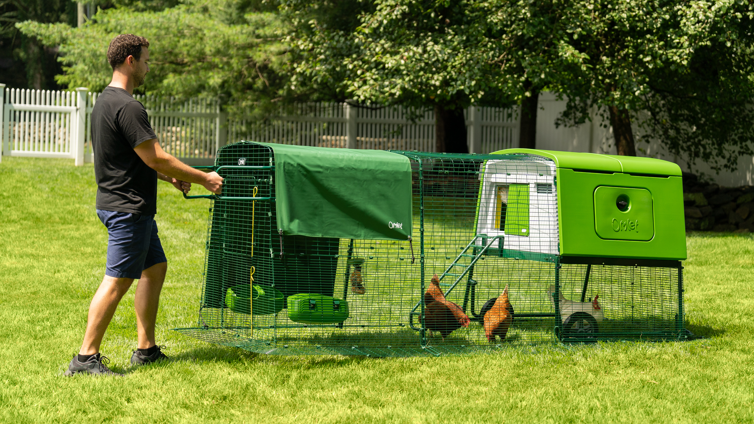 Man wheeling large Eglu Cube chicken coop and run easily across the backyard.